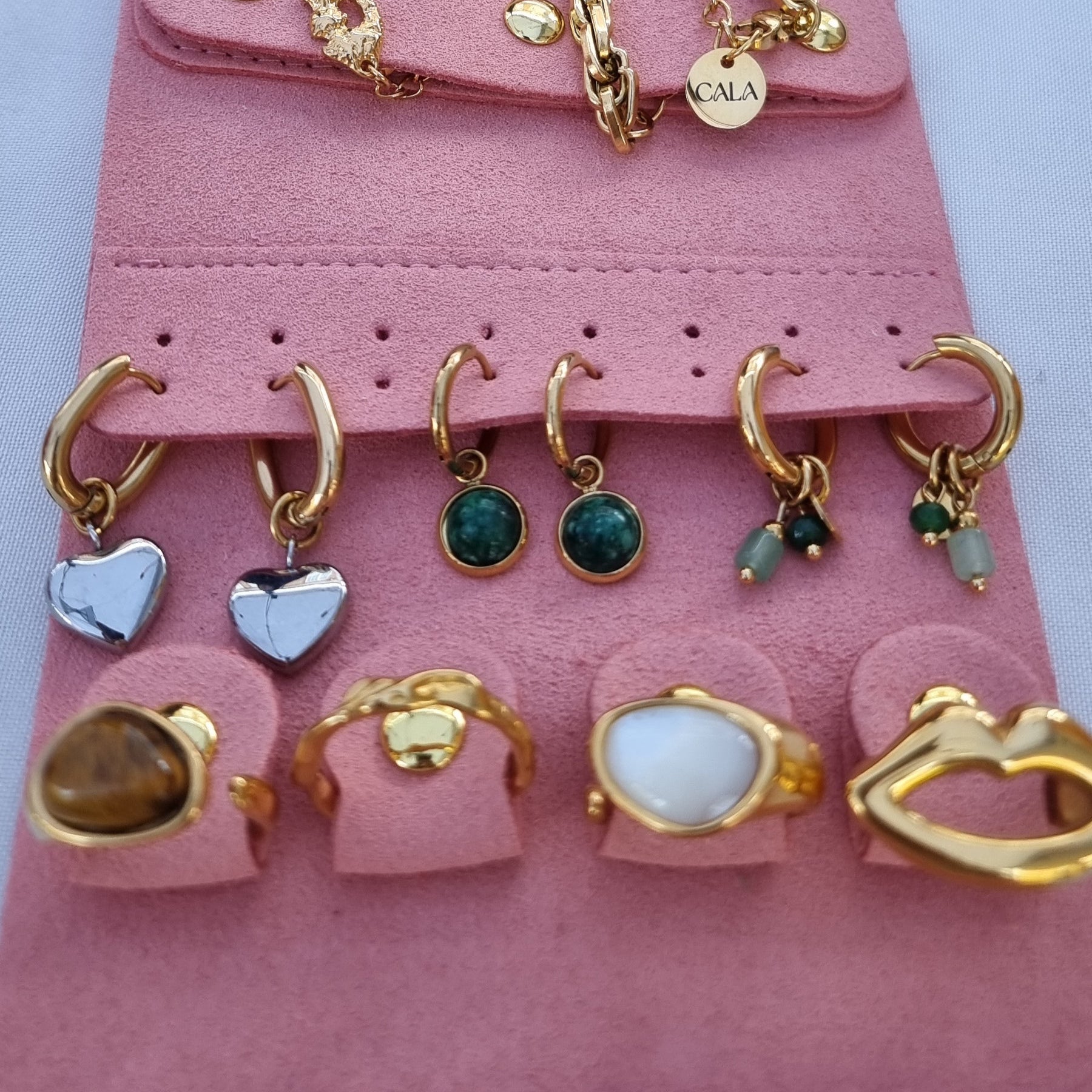 Pink jewelry roll with gold and silver jewelry on a white background