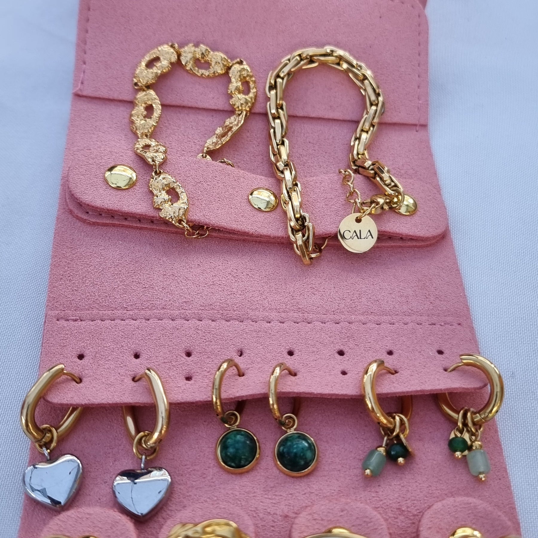 Pink jewelry roll with gold and silver jewelry on a white background